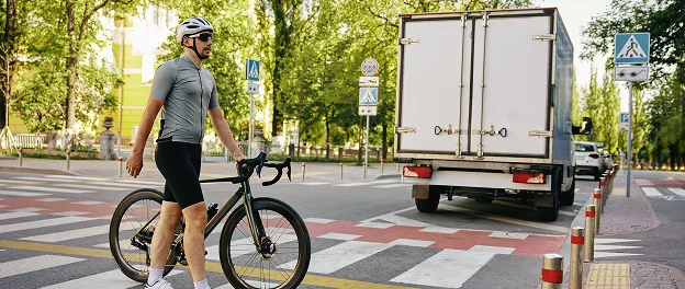 Ciclista cruzando una intersección junto a un camión y una zona peatonal.