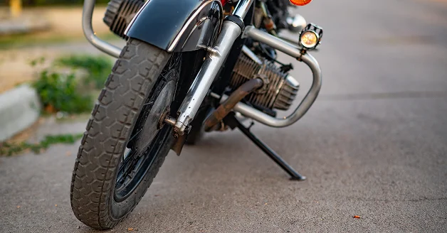 Motocicleta estacionada en la calle, vista de su rueda delantera y motor.