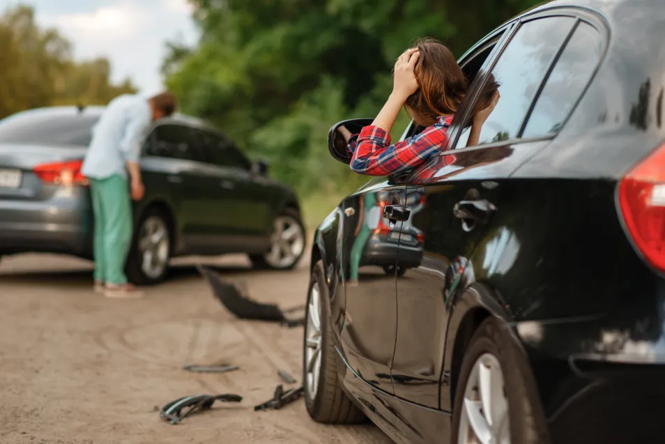 Mujer angustiada tras un accidente automovilístico con el vehículo dañado.