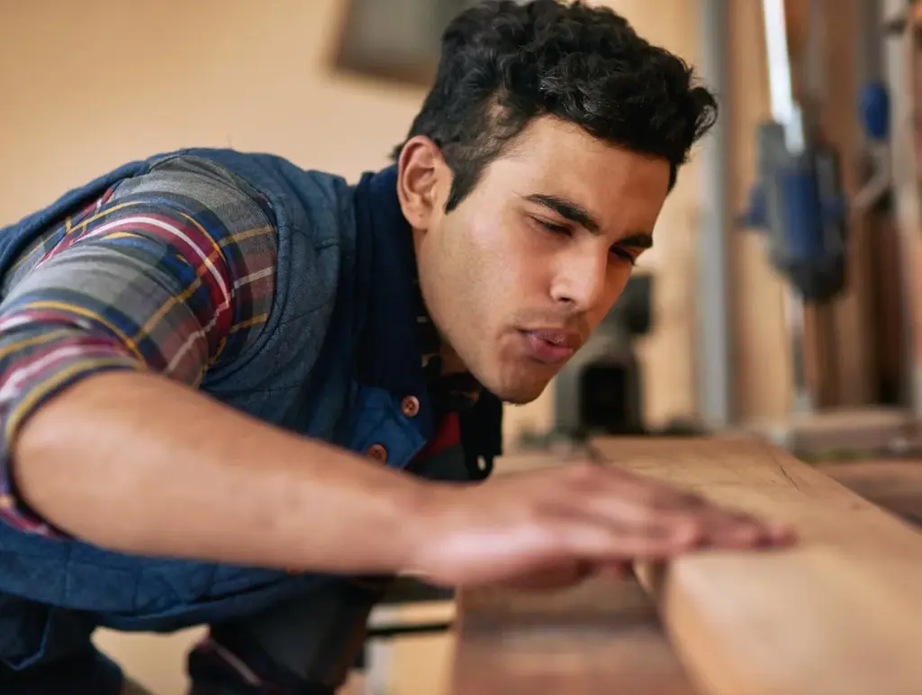Carpintero revisando con la mano la superficie de una tabla de madera en un taller.