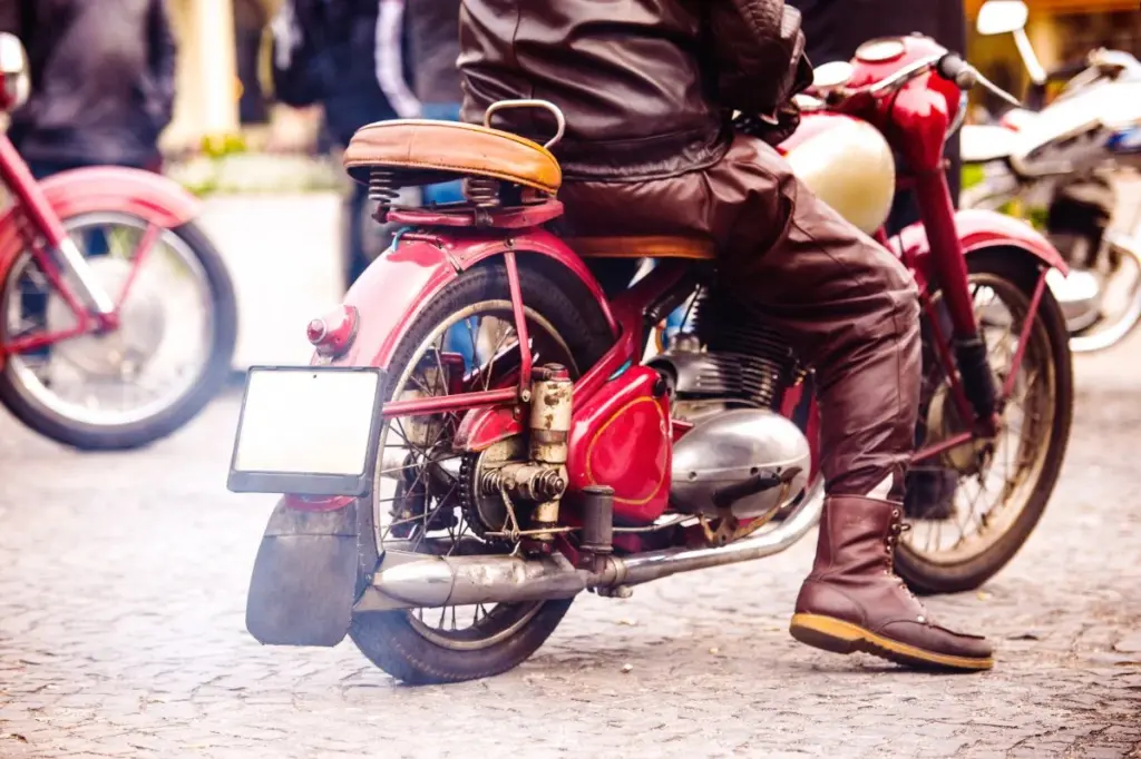 Motociclista con ropa de cuero sobre una motocicleta clásica roja en una calle empedrada.