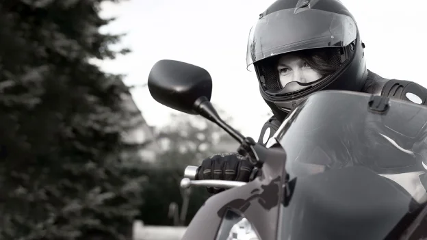 Motociclista con casco y guantes sobre una motocicleta deportiva, en blanco y negro.